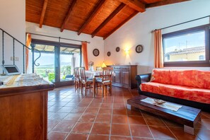 A spacious room with a wooden ceiling, a dining area with chairs and a table, a sofa, and a view through a large window. - Villa 'Sofia' with Mountain View, Wi-Fi and Air Conditioning (Punta de Su Turrione)