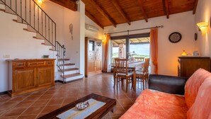 A spacious living area with a wooden staircase, a dining table with chairs, a sofa, and a view of the outdoors. - Villa 'Sofia' with Mountain View, Wi-Fi and Air Conditioning (Punta de Su Turrione)