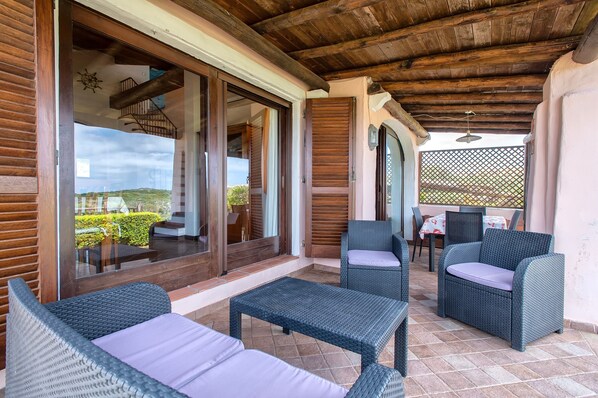 A covered outdoor seating area with wicker furniture, a view of the landscape, and a wooden ceiling.