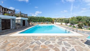 A swimming pool with stone flooring, a wooden deck, and a view of a hillside. - Villa 'Sofia' with Mountain View, Wi-Fi and Air Conditioning (Punta de Su Turrione)