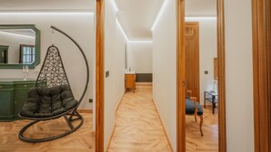 A hallway with a wooden floor, a hanging chair, a mirror, and a door leading to another room.