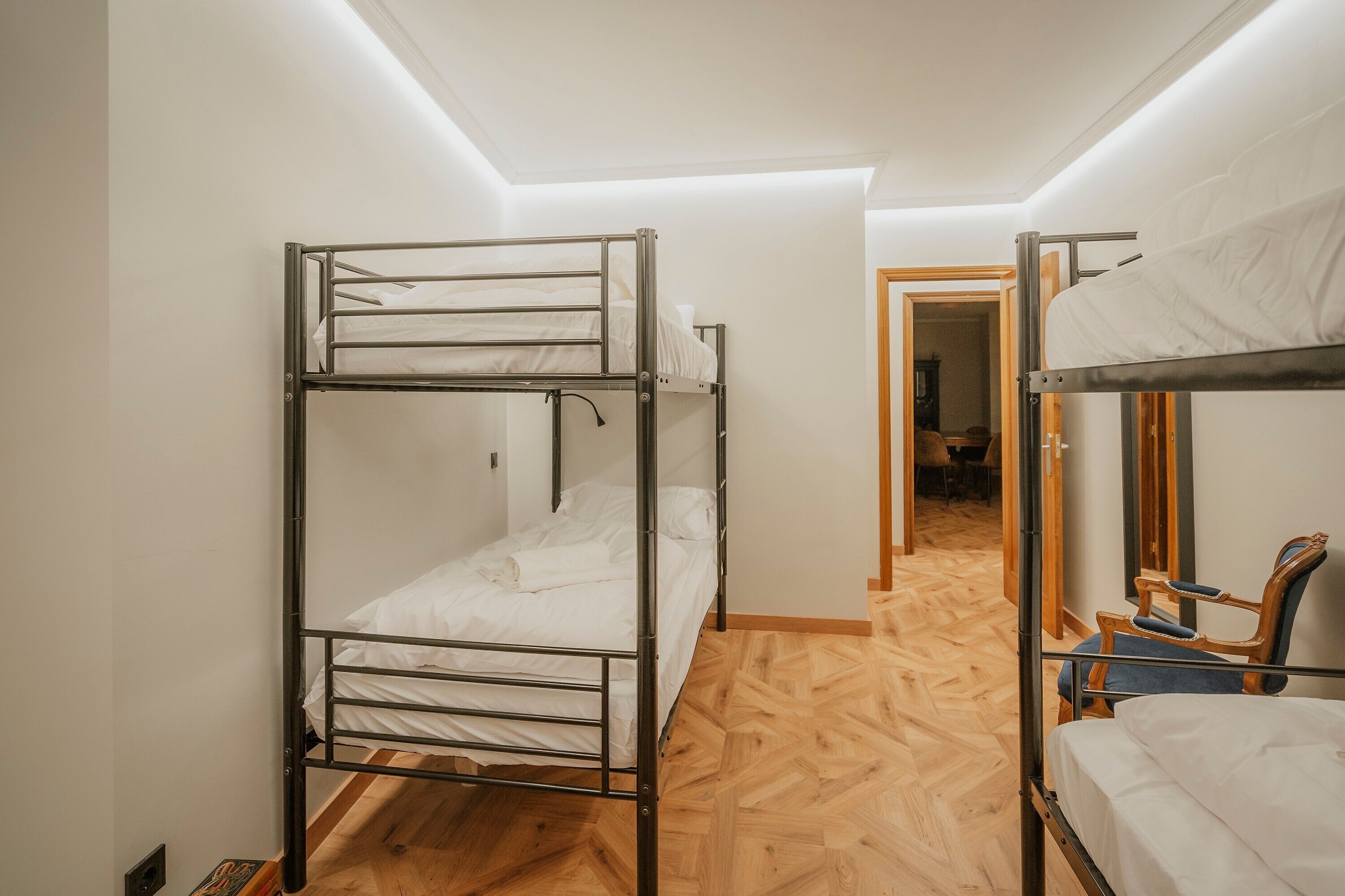 Dormitorio con literas, piso de madera, una puerta que da a otra habitación y una silla.