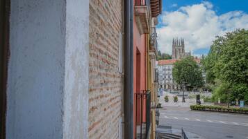 Vista de una calle con un edificio histórico al fondo, cielo despejado y aceras arboladas.