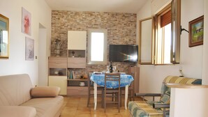 A living room with a sofa, a dining table with chairs, a TV, and a window.