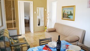 A dining area with a table set for two, a sofa, and a painting on the wall.