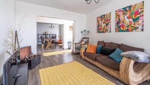 A living room with a brown sofa, yellow rug, and two colorful wall paintings. - Country House 'Serrão' with Private Terrace, Private Garden and Wi-Fi (Calheta)