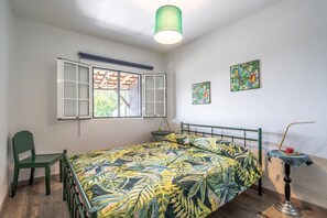 Une chambre à coucher avec un lit, une chaise, une table avec une lampe et deux tableaux accrochés au mur.