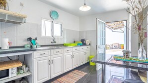 A modern kitchen with white cabinets, a black countertop, a clock, and a window. - Country House 'Serrão' with Private Terrace, Private Garden and Wi-Fi (Calheta)