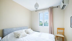 Et soveværelse med seng, stol, vindue med gardiner, et klimaanlæg og en hængende lampe.