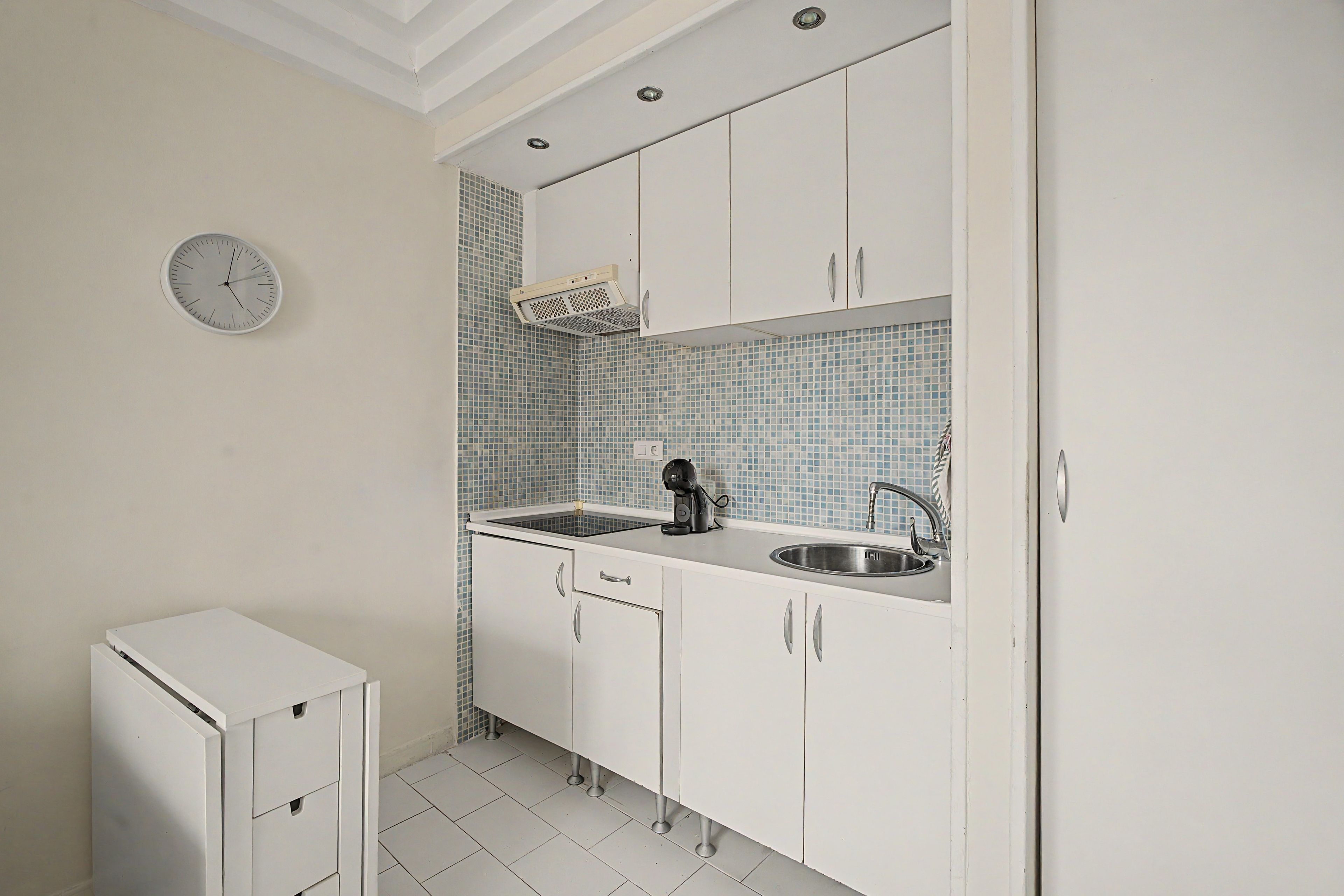 Una cocina compacta con armarios blancos, un lavamanos y un reloj en la pared.