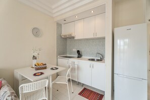 Une cuisine de taille réduite avec des meubles blancs, un évier, une cuisinière et un réfrigérateur.