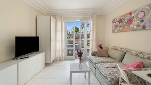 A living room with a TV, sofa, and a painting on the wall. - Vacation Apartment 'Complejo 206' with Sea View, Shared Pool and Wi-Fi (Costa Adeje)