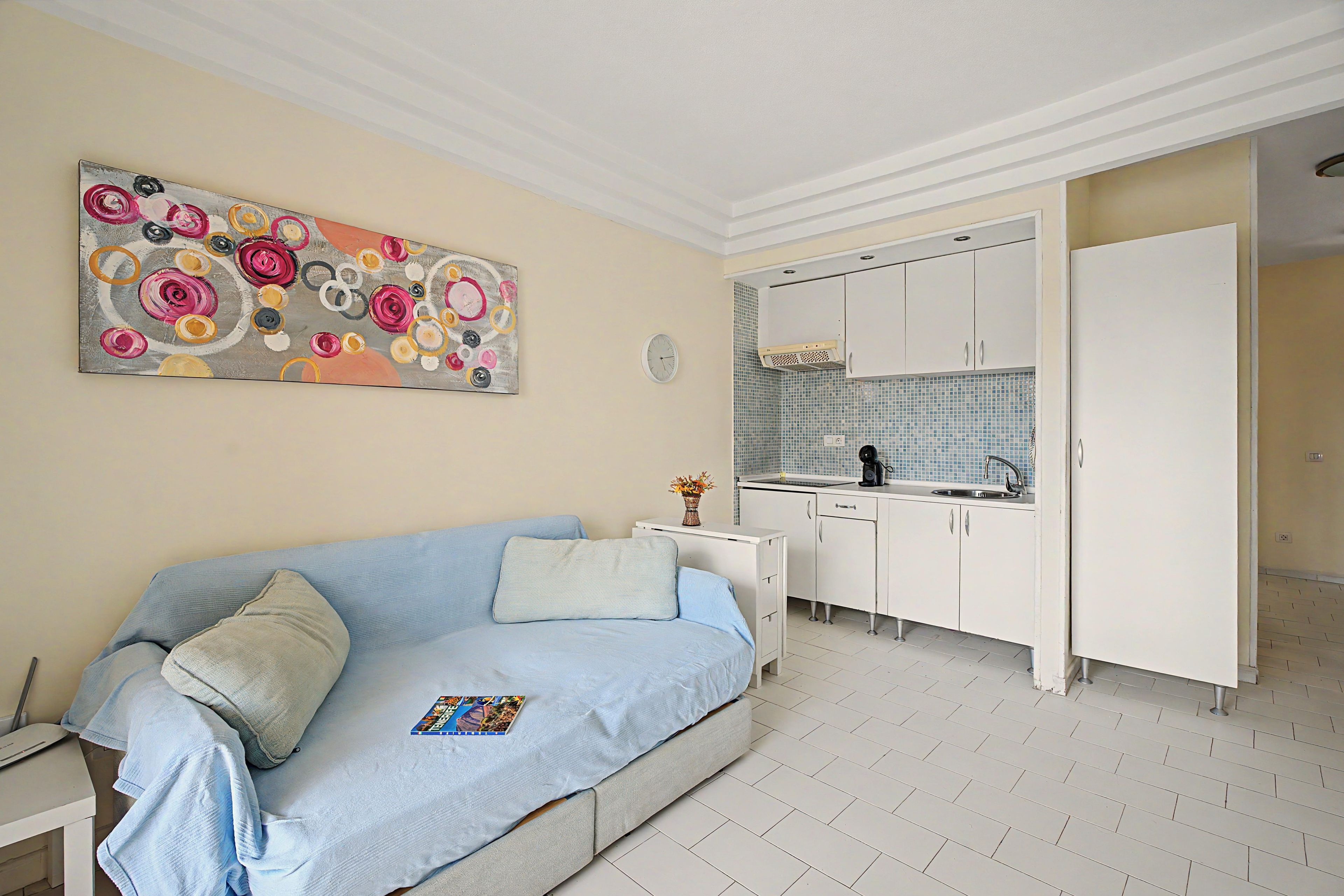 A room with a sofa, a kitchen area, and a decorative painting.