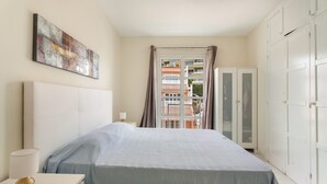 A bedroom with a bed, a bedside table with a lamp, a wall-mounted abstract painting, and a view of a balcony through a door. - Vacation Apartment 'Complejo 206' with Sea View, Shared Pool and Wi-Fi (Costa Adeje)