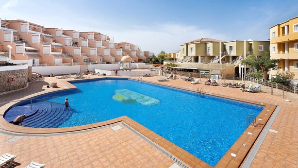 A swimming pool with a tiled deck, lounge chairs, and a building with balconies in the background. - Vacation Apartment 'Complejo 206' with Sea View, Shared Pool and Wi-Fi (Costa Adeje)