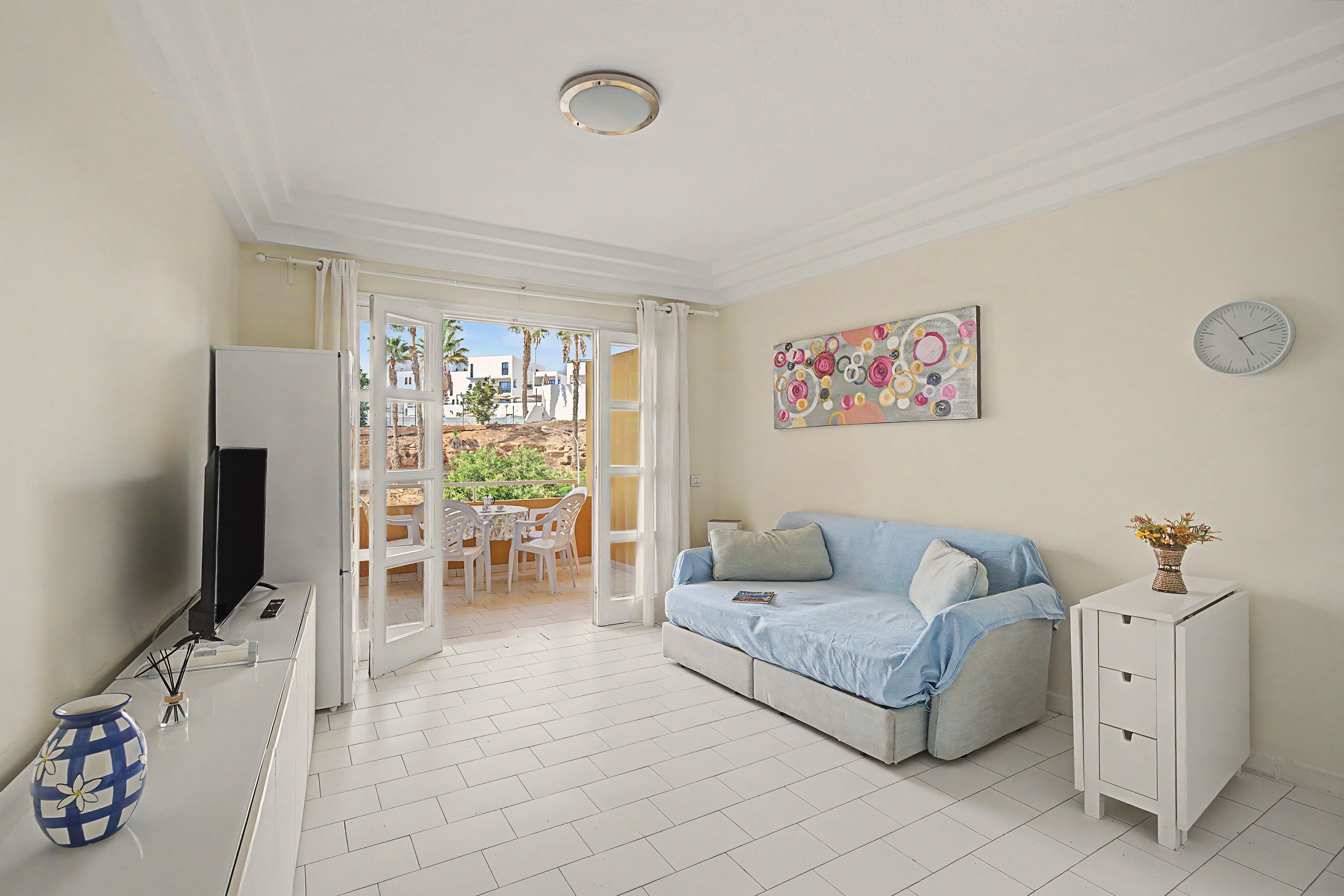 A room with a sofa, a TV, a small cabinet, a vase with flowers, and a painting on the wall.