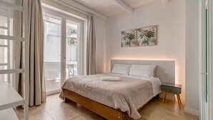 Une chambre à coucher comprenant un lit, une table de chevet, une fenêtre avec des rideaux et une œuvre d’art accrochée au mur.