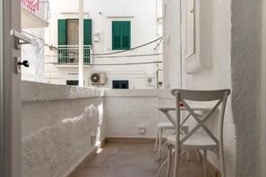 A narrow balcony with white walls, a white chair, and a small table.