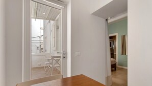 Une pièce avec une table en bois, une porte blanche donnant sur un balcon et un lit avec une tête de lit de couleur claire.