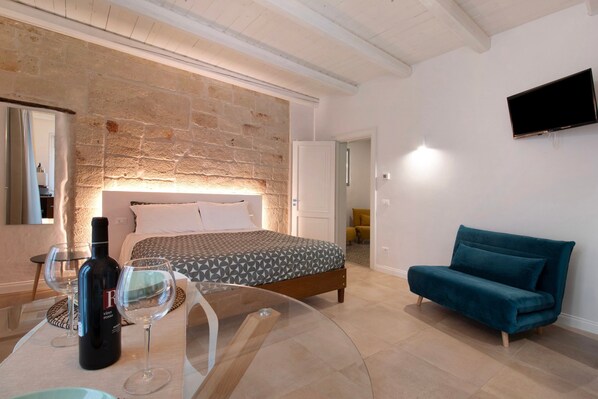 Un dormitorio con pared de piedra, cama, televisor, sofá y mesa con una botella y vasos.