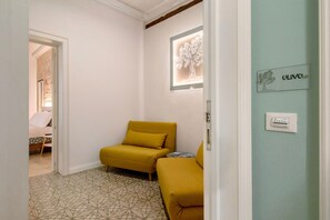 Une pièce avec un sol à motifs, un fauteuil jaune, une petite table et un luminaire fixé au mur.