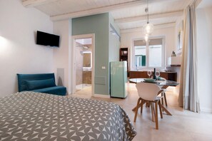 Une chambre d’h ôtel moderne avec un grand lit, un téléviseur fixé au mur, un coin repas avec une table et des chaises, et une cuisine à l’arrière-plan.