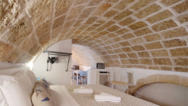 A cozy room with a brick ceiling, a bed with white linens, a desk with a chair, and a small table with a chair. - Apartment 'Pescatore' with Wi-Fi and Air Conditioning (Monopoli)