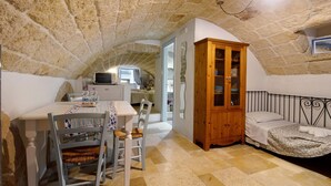 A room with a stone ceiling, a wooden cabinet, a bed, and a dining area with a table and chairs. - Apartment 'Pescatore' with Wi-Fi and Air Conditioning (Monopoli)