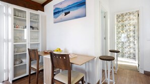 Un coin repas avec une table en bois, deux chaises, un saladier rempli de fruits et un tableau représentant un paysage lacustre accroché au mur.