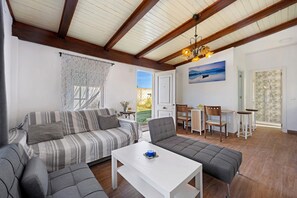 A living room with a sofa, armchair, and a white table. There is a dining area with chairs and a table. The room has wooden beams on the ceiling and a painting on the wall. - Holiday Home 'Manoli' with Private Pool, Wi-Fi and Air Conditioning (Chiclana de la Frontera)