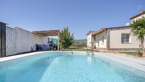 Une piscine agrémentée d’une pergola, un espace barbecue couvert et un bâtiment en pierre avec un toit rouge.