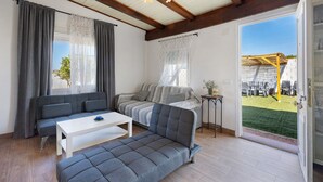Un salon moderne avec un canapé, une table basse blanche et une vue sur un jardin extérieur.