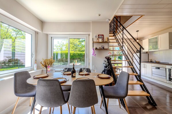 A modern dining area with a round table, grey chairs, and a view of the outdoors.