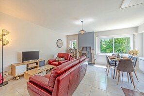 A modern living room with a red sofa, a flat-screen TV, a fireplace, and a dining area with chairs.