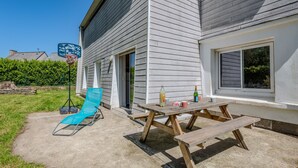 A patio with a wooden table and benches, a blue chair, and a basketball hoop.