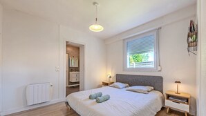 A bedroom with a bed, bedside tables, a radiator, a window with blinds, and a hanging light fixture.