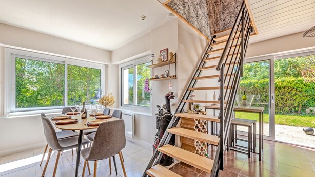 A modern interior with a dining area, a staircase, and a view of greenery outside.