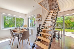 A modern interior with a dining area, a staircase, and a view of greenery outside. - Holiday Home 'La Maison De Kerscovie' with Private Terrace, Private Garden and Wi-Fi (Morlaix)