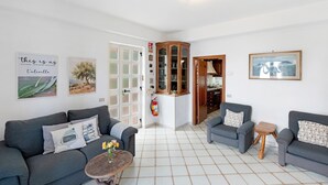 Una sala de estar con dos sofás, una mesita con flores, un aparador y una puerta que da a otra habitación.