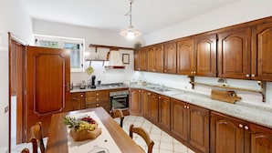 Cocina con gabinetes de madera, encimera de granito, mesa de comedor con sillas y lámpara colgante.