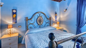 A bedroom with a blue wall, a bed with a decorative headboard, bedside lamps, and a wooden nightstand. - Apartment 'Merlot, 4' with Private Garden and Wi-Fi (Montefalco)