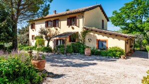 A two-story house with a gravel driveway, surrounded by potted plants and trees. - Apartment 'Merlot, 4' with Private Garden and Wi-Fi (Montefalco)