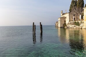 A calm body of water with clear visibility, a historic building with a flag, and a tree on the right.