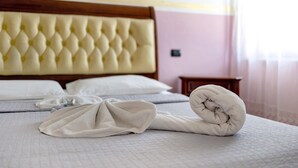 Een net opgemaakt bed met een gebonden hoofdbord, een opgerolde handdoek en een nachtkastje.