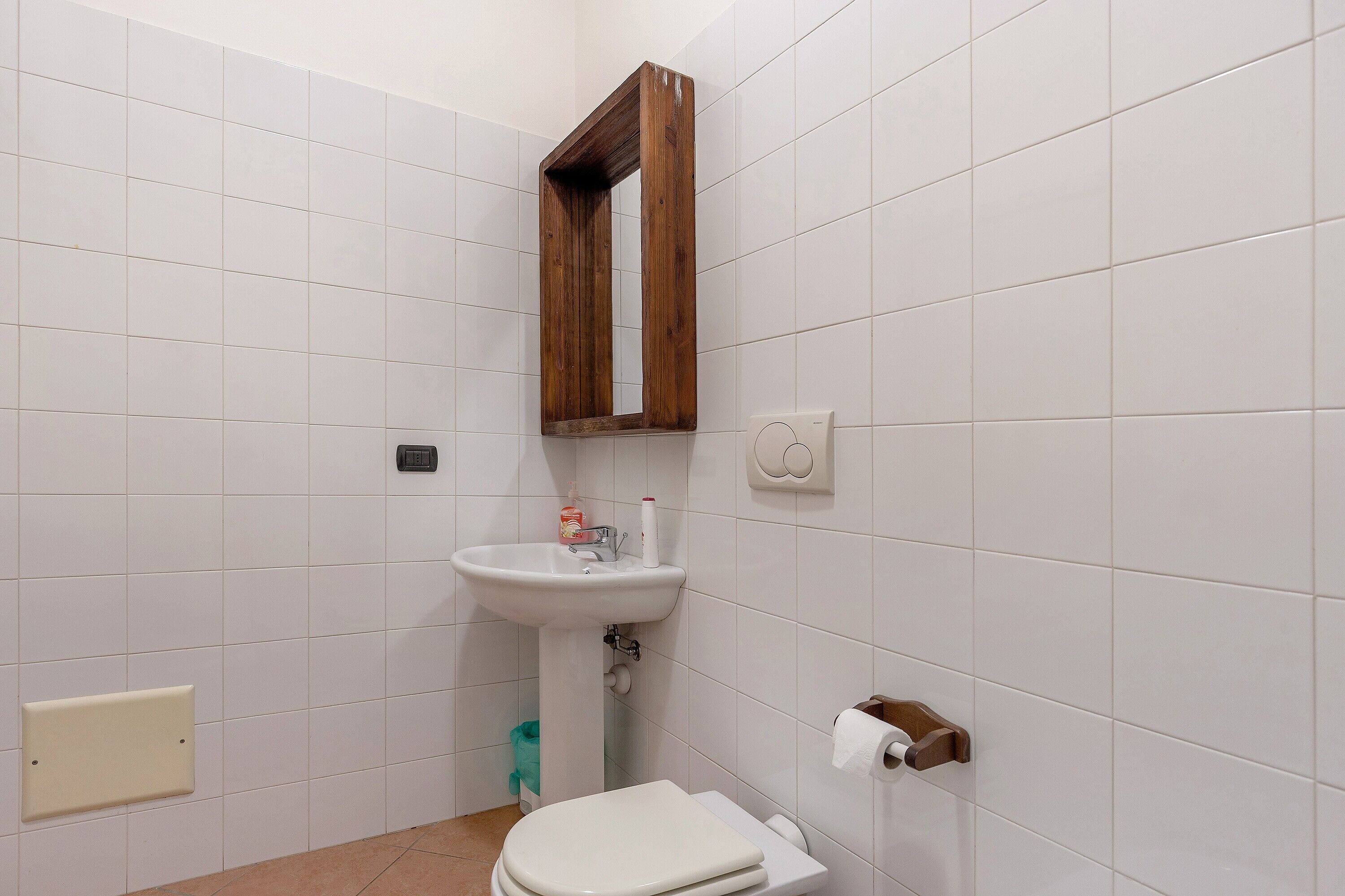A bathroom with white tiles, a wooden-framed mirror, a white sink, and a toilet.
