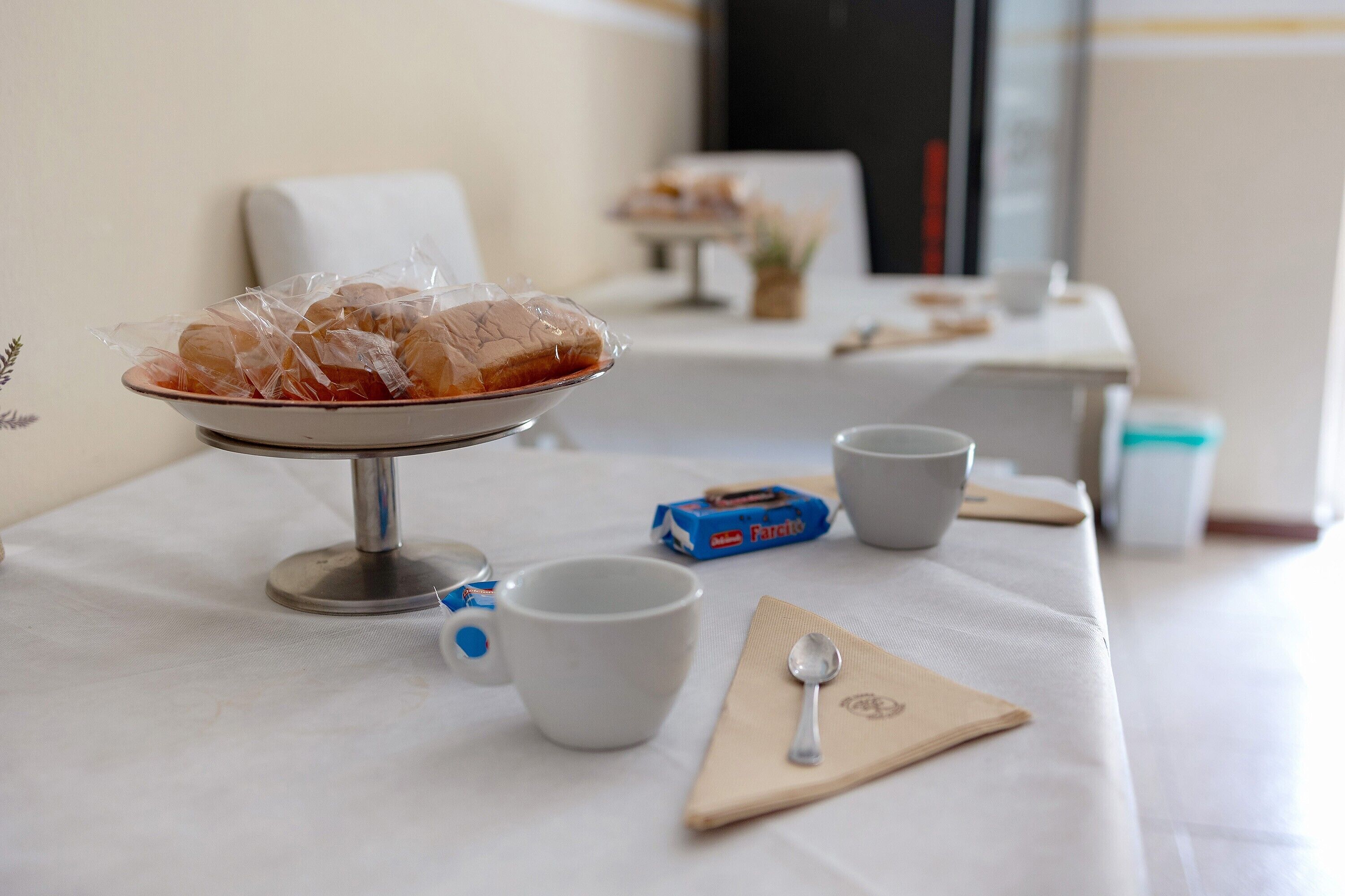 A breakfast setup with a bowl of pastries, a cup, a napkin, a spoon, and a box of Farico.