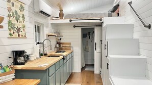 A modern kitchen with a wooden countertop, a built-in sink, and a small island. There is a hanging plant and a whiteboard on the wall. - The Tiny with Big Time Vibes and Walkability (Austin)