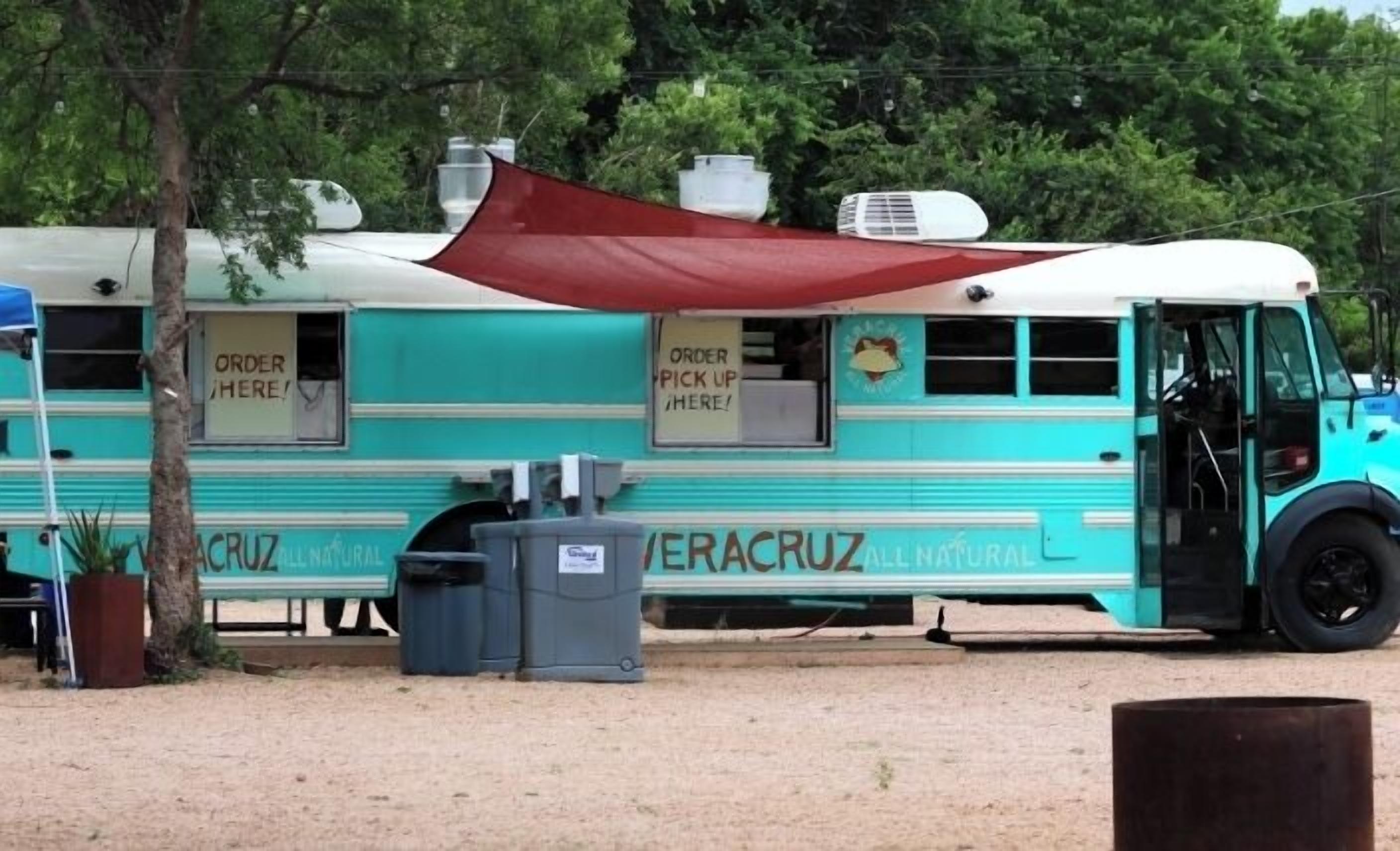 Ein türkisfarbener Food-Truck mit der Beschriftung 'ERACRUZ ALL NATURAL', einem roten Verdeck und einer Mülltonne.
