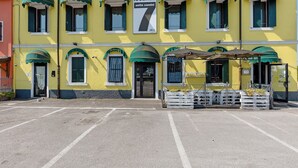 A yellow building with green awnings, a sign reading 'locanda sette camini,' and a parking lot in front.