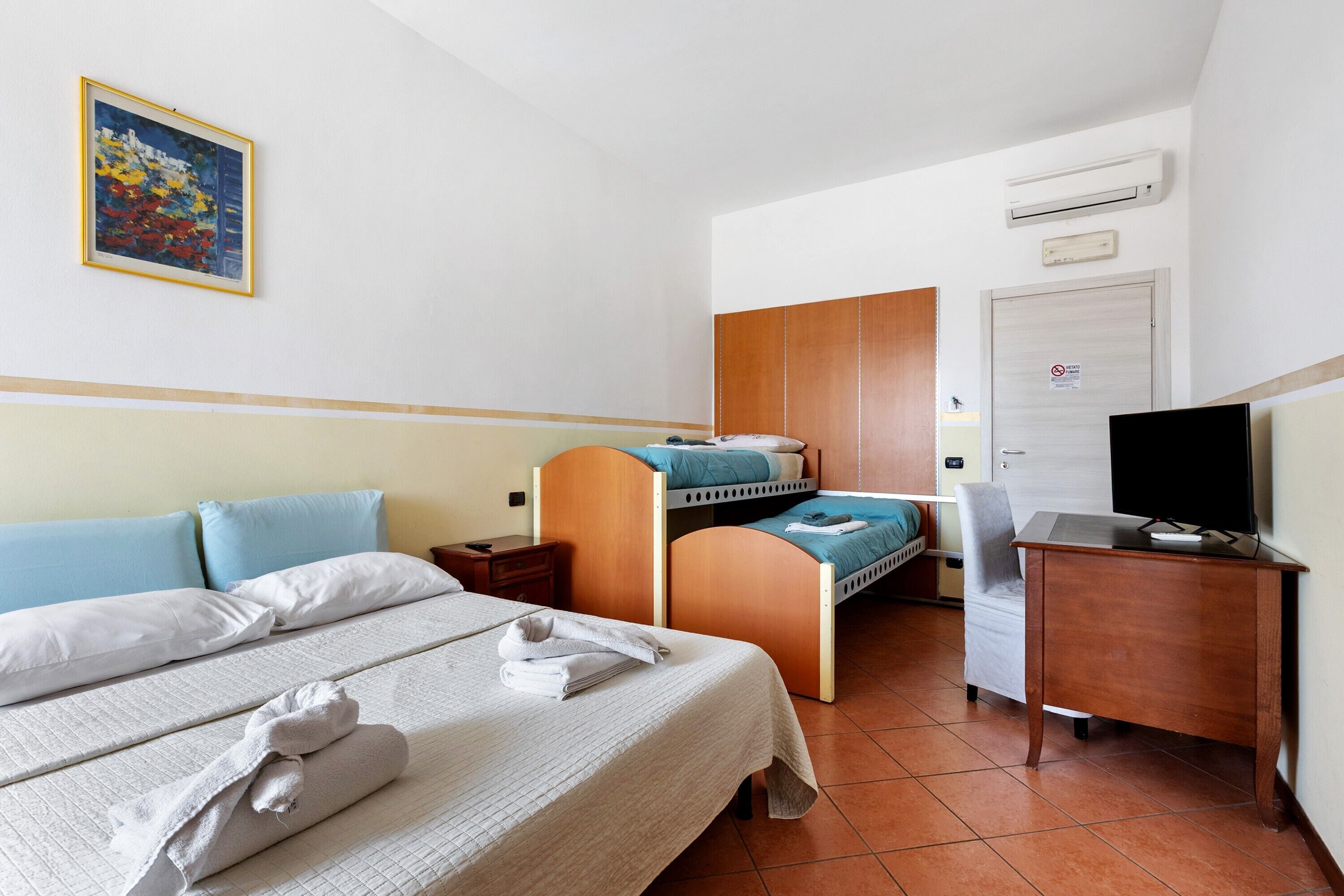 A hotel room with a bed, a desk, a chair, a television, and a wardrobe.